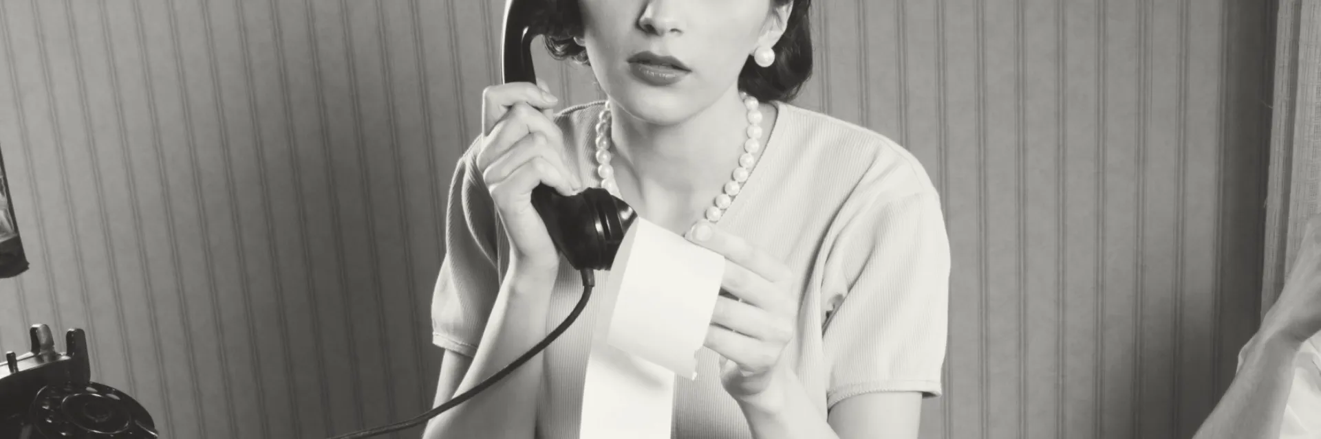 Image d'illustration des coûts de fonctionnement annuel du service Attraction - Jeune femme au téléphone dans les années 50 qui regarde le détail d'un rouleau d'impression d'une calculatrice - Photo noir et blanc